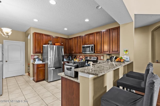 kitchen featuring a textured ceiling, stainless steel appliances, light stone counters, and kitchen peninsula