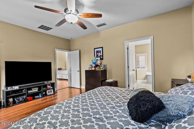 bedroom with a textured ceiling, ceiling fan, ensuite bath, and light wood-type flooring