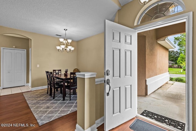 foyer entrance with a textured ceiling, light hardwood / wood-style flooring, a notable chandelier, and a wealth of natural light