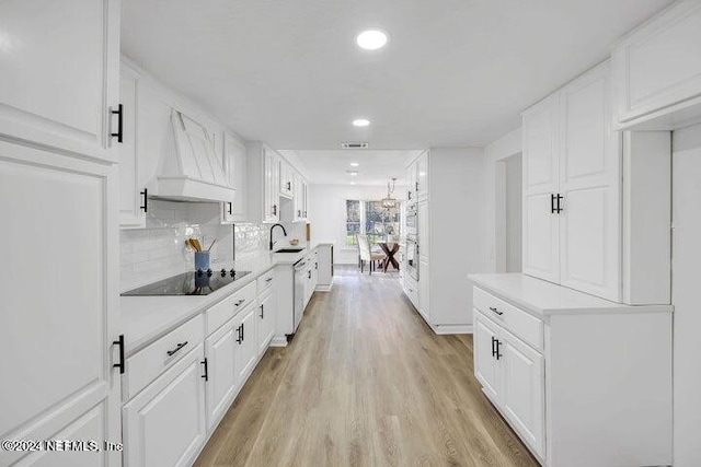 kitchen with custom range hood, black electric stovetop, light wood-type flooring, and white cabinets