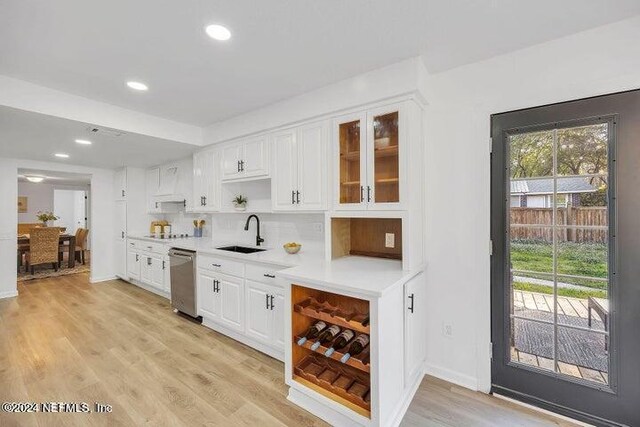 bar featuring sink, decorative backsplash, light hardwood / wood-style floors, dishwasher, and white cabinets