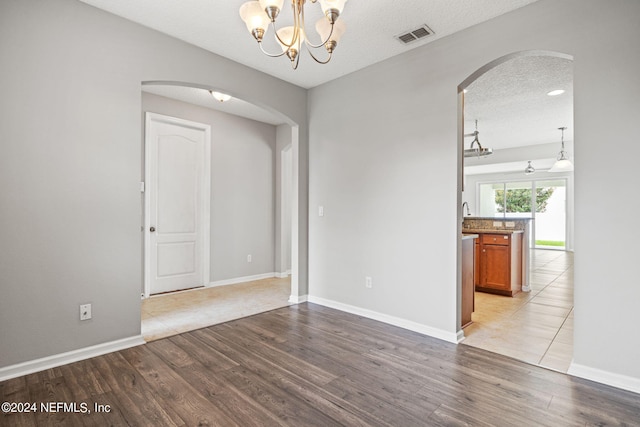 unfurnished room with a chandelier, a textured ceiling, and light hardwood / wood-style flooring