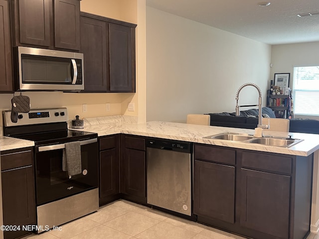 kitchen featuring appliances with stainless steel finishes, dark brown cabinets, light tile patterned floors, sink, and kitchen peninsula