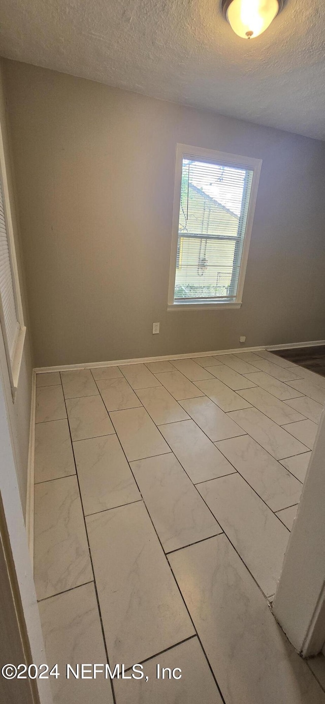 unfurnished room with baseboards and a textured ceiling