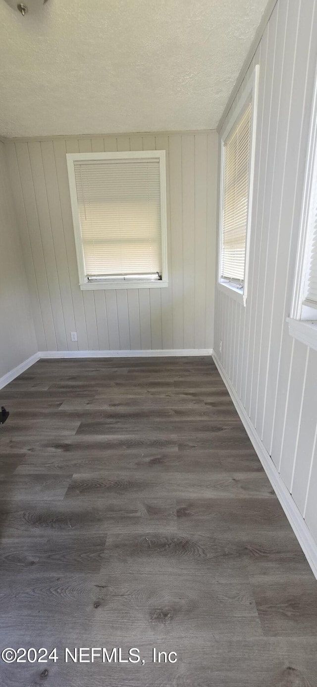 empty room with dark wood-style floors, a textured ceiling, and baseboards