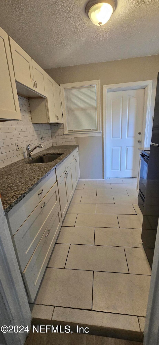 kitchen with a textured ceiling, backsplash, white cabinets, sink, and dark stone counters