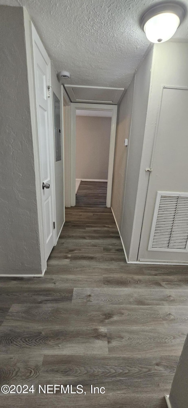 corridor with electric panel, visible vents, a textured wall, wood finished floors, and a textured ceiling