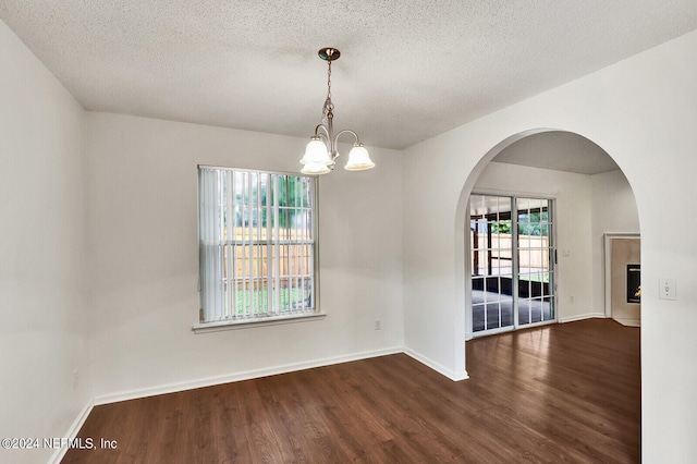 spare room featuring an inviting chandelier, dark wood-type flooring, a textured ceiling, and a healthy amount of sunlight