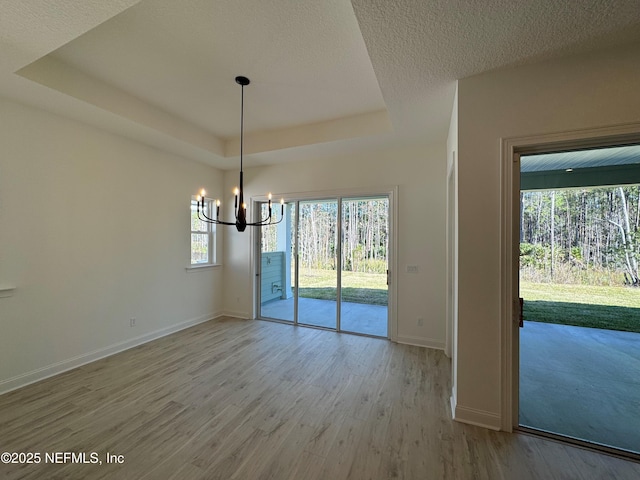 unfurnished dining area with an inviting chandelier, a tray ceiling, light hardwood / wood-style floors, and a textured ceiling