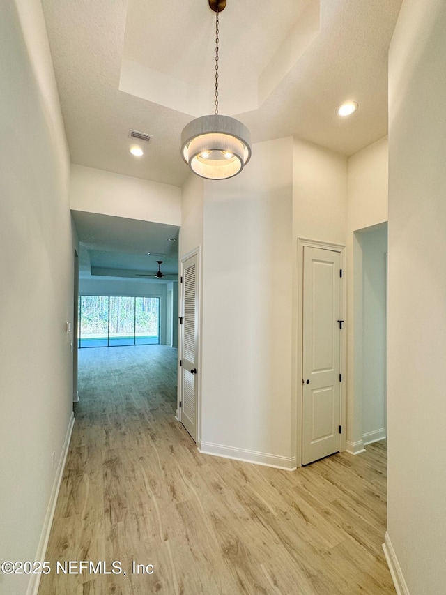 corridor with light hardwood / wood-style floors and a raised ceiling