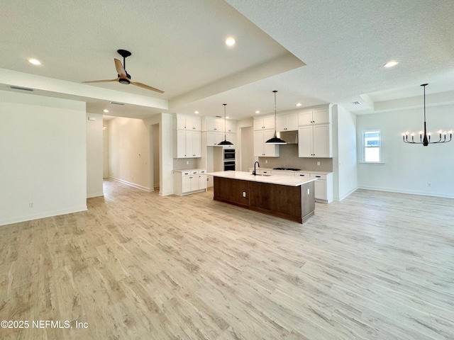 kitchen with a tray ceiling, white cabinets, decorative light fixtures, a large island with sink, and light wood-type flooring