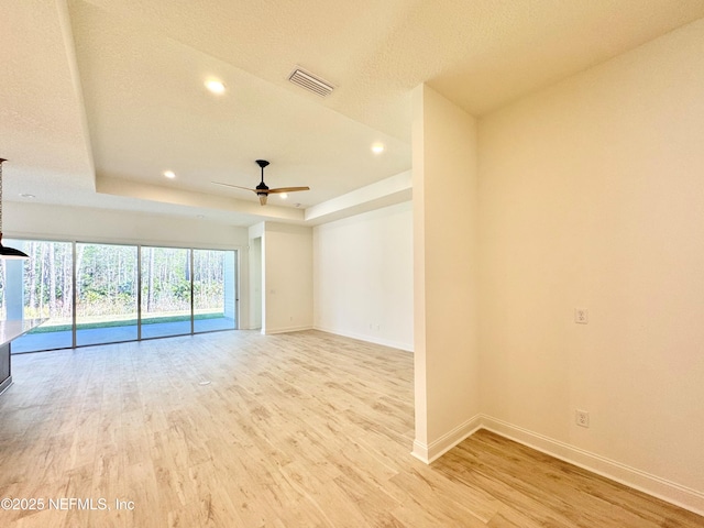 spare room with a raised ceiling, ceiling fan, and light hardwood / wood-style floors