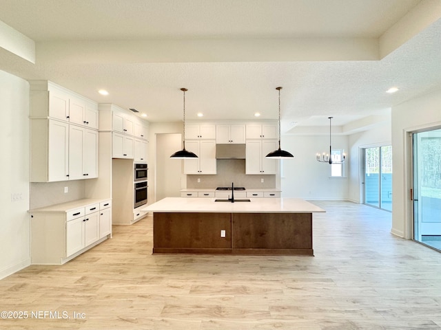 kitchen featuring pendant lighting, a center island with sink, and white cabinets