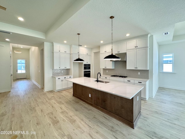 kitchen with sink, gas stovetop, white cabinetry, a center island with sink, and pendant lighting