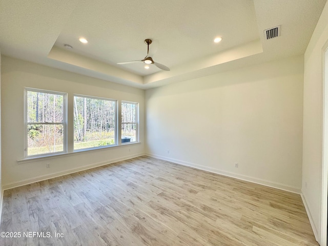 empty room featuring a raised ceiling, ceiling fan, and light hardwood / wood-style floors