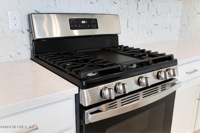 interior details with gas range, white cabinetry, and decorative backsplash