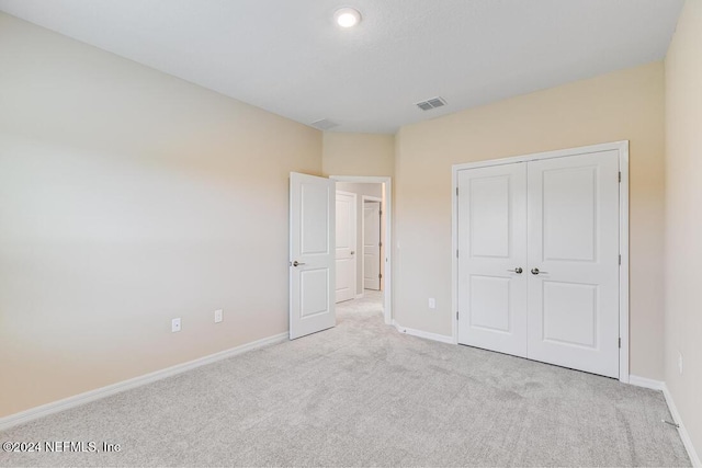 unfurnished bedroom with light colored carpet and a closet