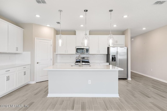 kitchen with pendant lighting, appliances with stainless steel finishes, white cabinetry, and an island with sink