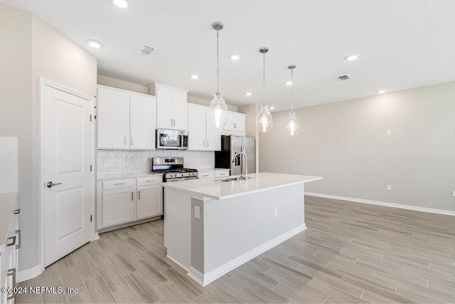 kitchen with sink, decorative light fixtures, stainless steel appliances, a kitchen island with sink, and white cabinets