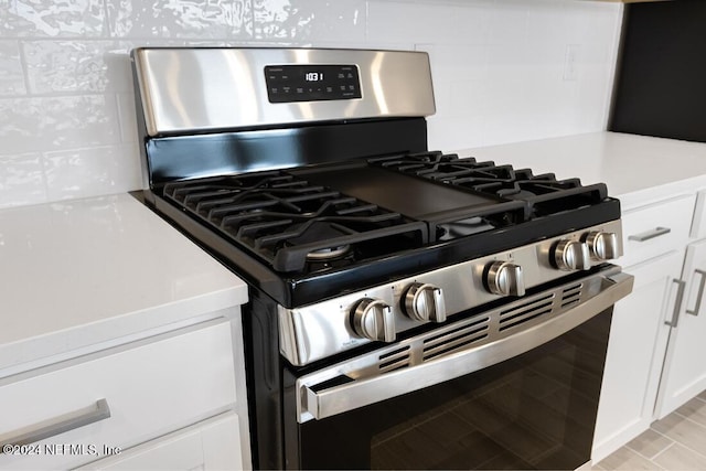 interior details featuring tasteful backsplash, gas stove, and white cabinets