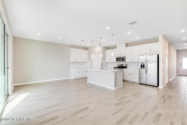 kitchen featuring white cabinets, hanging light fixtures, an island with sink, light wood-type flooring, and appliances with stainless steel finishes