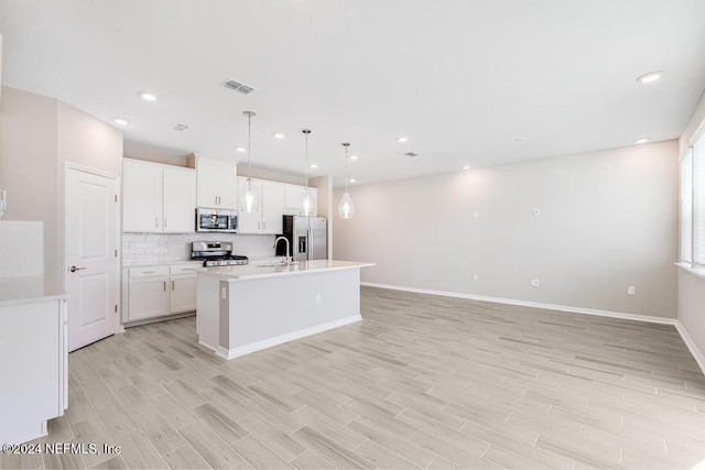 kitchen with light hardwood / wood-style flooring, appliances with stainless steel finishes, a kitchen island with sink, hanging light fixtures, and white cabinets