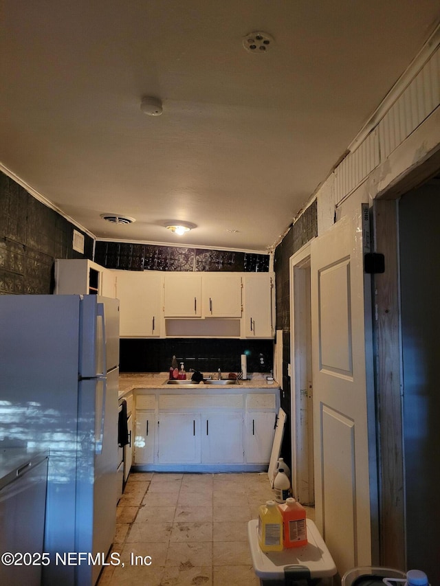 kitchen featuring a sink, visible vents, white cabinetry, light countertops, and freestanding refrigerator