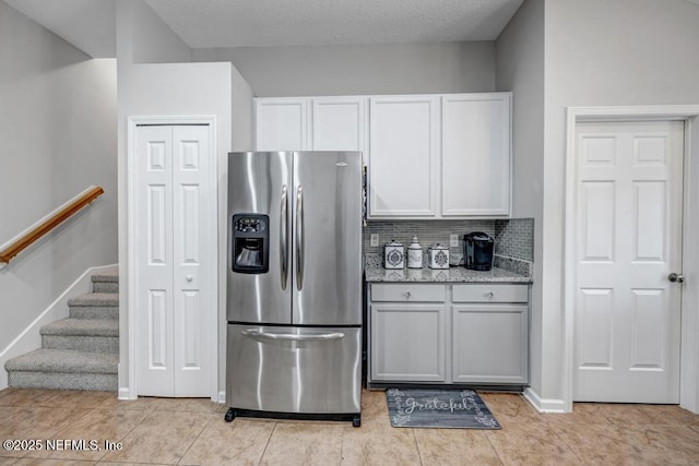 kitchen with tasteful backsplash, white cabinets, light tile patterned floors, light stone counters, and stainless steel fridge with ice dispenser