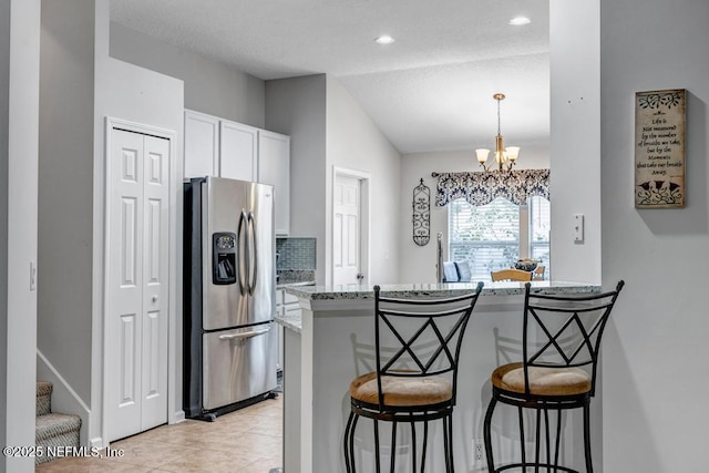 kitchen featuring white cabinetry, a kitchen breakfast bar, stainless steel refrigerator with ice dispenser, light stone countertops, and kitchen peninsula