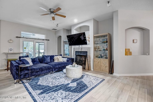 living room with a tiled fireplace, ceiling fan, and light wood-type flooring