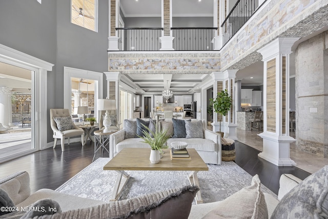 living room featuring dark wood-type flooring, coffered ceiling, a towering ceiling, decorative columns, and crown molding