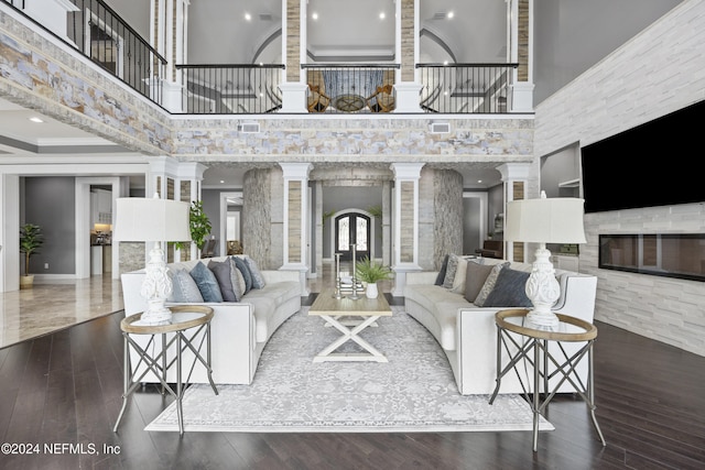 living area featuring dark wood finished floors, decorative columns, visible vents, a towering ceiling, and a glass covered fireplace