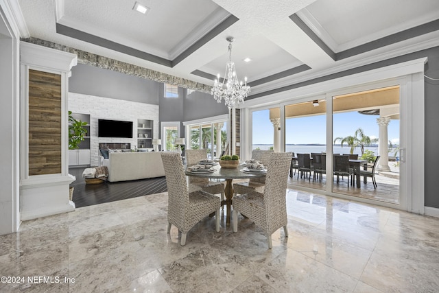 dining space featuring a textured ceiling, a stone fireplace, marble finish floor, ornamental molding, and an inviting chandelier