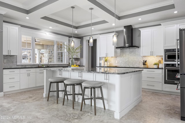 kitchen with wall chimney exhaust hood, a kitchen island, and white cabinets