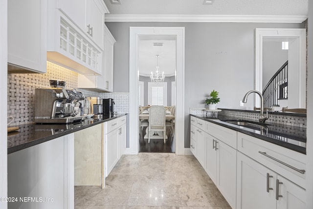 kitchen with dark stone counters, ornamental molding, a sink, and white cabinets