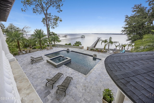 pool with a patio area, a water view, and an in ground hot tub