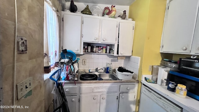 kitchen with tasteful backsplash, light countertops, white cabinets, white dishwasher, and a sink