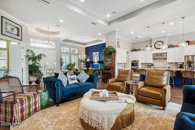 living room featuring light hardwood / wood-style floors, a raised ceiling, an inviting chandelier, and ornamental molding