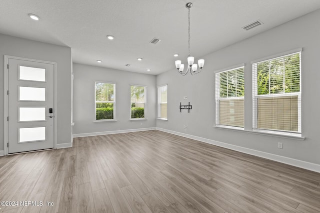 foyer featuring light wood-type flooring, an inviting chandelier, a textured ceiling, and a wealth of natural light