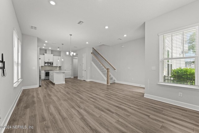 unfurnished living room featuring light wood-type flooring, an inviting chandelier, and a healthy amount of sunlight