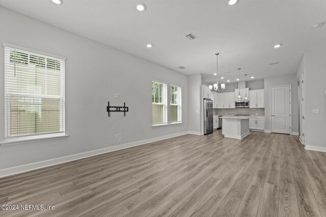 unfurnished living room featuring light wood-type flooring and a notable chandelier