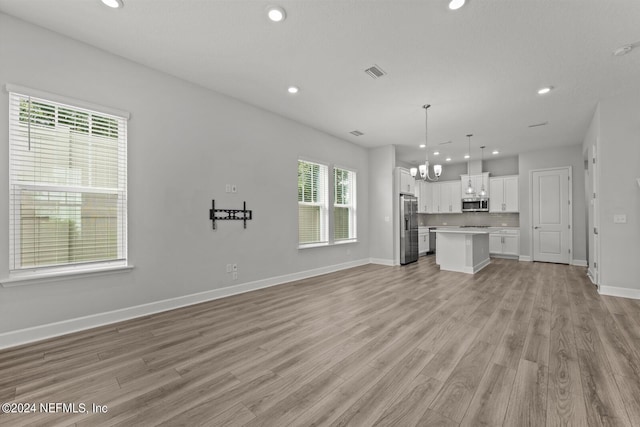 unfurnished living room with light wood-type flooring and a chandelier