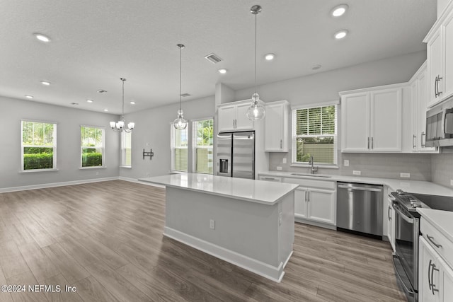 kitchen featuring appliances with stainless steel finishes, hanging light fixtures, white cabinets, a kitchen island, and sink