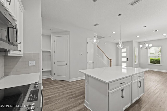 kitchen with decorative backsplash, white cabinetry, light wood-type flooring, a kitchen island, and hanging light fixtures