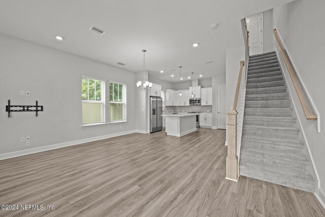 unfurnished living room with light wood-type flooring and a chandelier