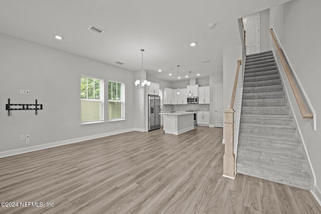 unfurnished living room with an inviting chandelier and light hardwood / wood-style flooring