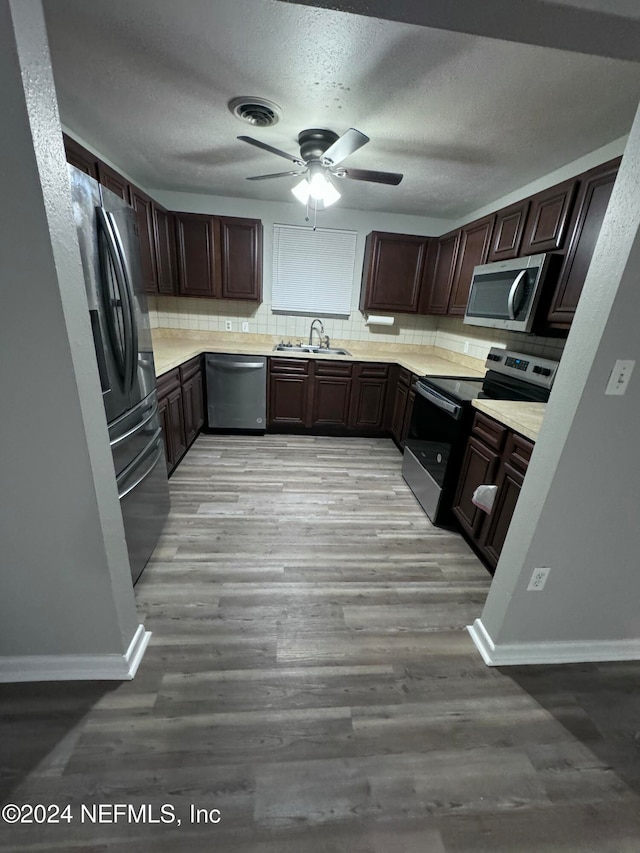 kitchen with dark brown cabinetry, decorative backsplash, stainless steel appliances, and light hardwood / wood-style floors