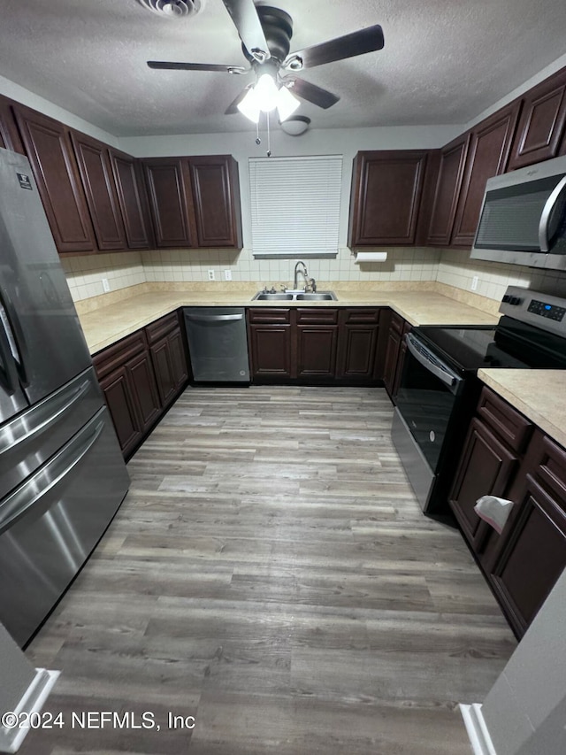 kitchen featuring appliances with stainless steel finishes, tasteful backsplash, ceiling fan, sink, and light hardwood / wood-style flooring