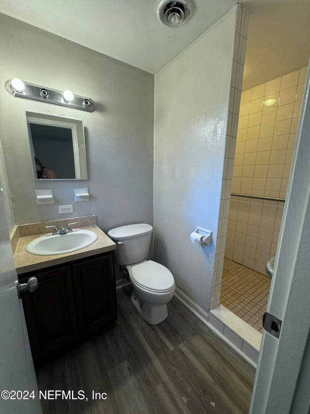 bathroom with a tile shower, vanity, hardwood / wood-style flooring, and toilet