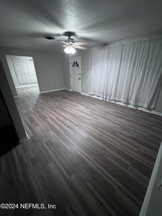 unfurnished living room featuring a textured ceiling, ceiling fan, and dark wood-type flooring